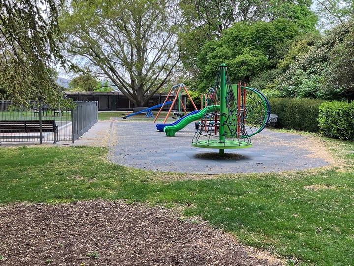 Park lawn with playground equipment and mature trees