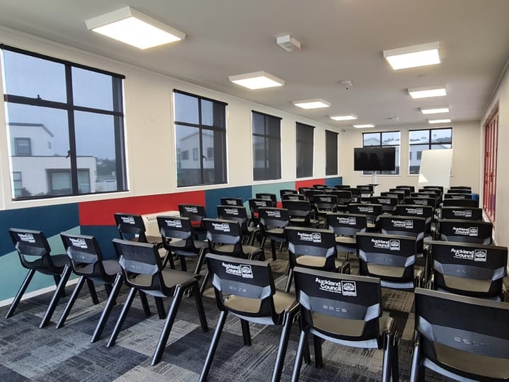 Room set with rows of chairs facing a screen and whiteboard