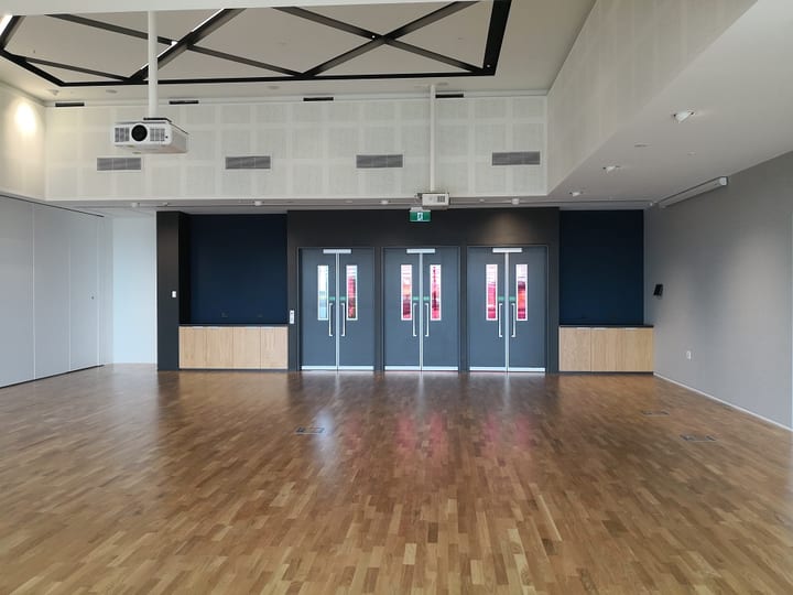 Large timber-floored hall with dark double doors, navy accent wall, geometric black ceiling detail