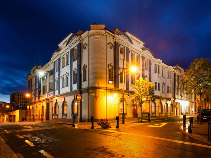 White heritage corner building with arched windows and ornate parapet, lit at night