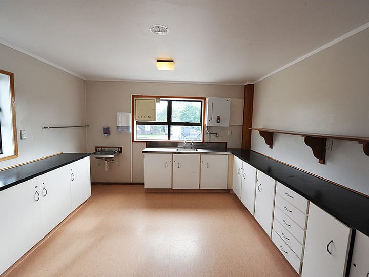 Larger kitchen with white cabinetry, dark benchtop, and window looking to car park