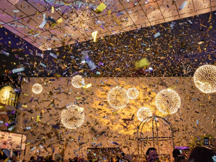Indoor event space filled with falling confetti, spherical pendant lights and warm uplighting