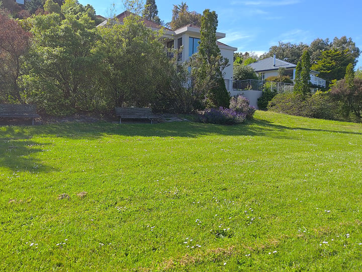 Grassed reserve with lawn, garden beds and residential buildings behind