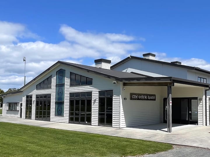 Large white and dark-trim barn building with stained-glass entry panels, open lawn