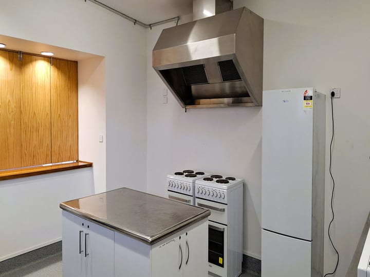 Compact kitchen with stainless steel benchtop, range hood, two ovens and upright fridge