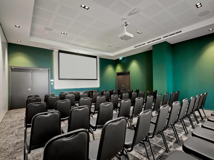 Function room with green accent walls, theatre-style black chairs, and a projection screen