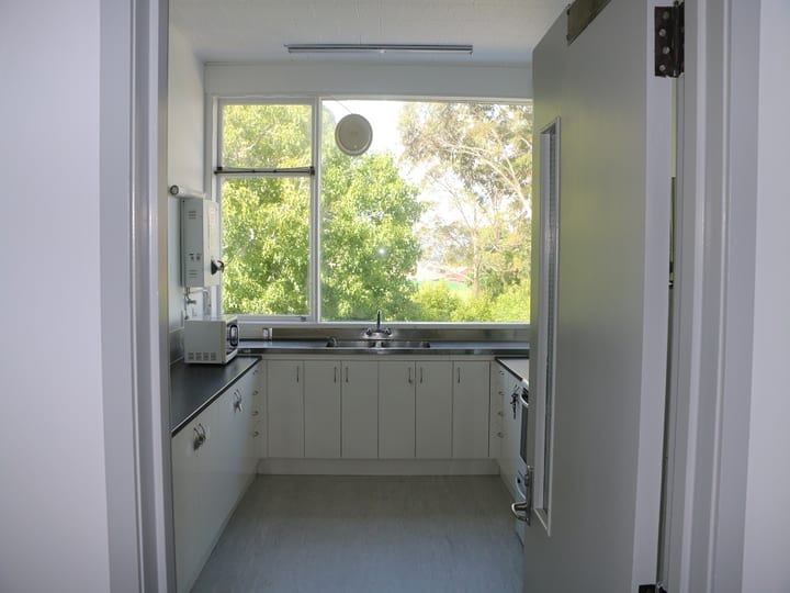 Small kitchen with white cabinetry, stainless sink, and window overlooking trees