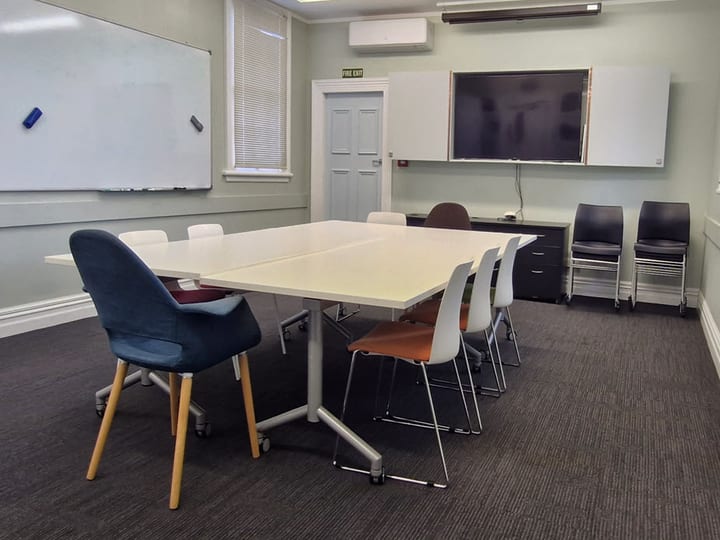 Small meeting room with mixed chairs, white tables, whiteboard and wall-mounted screen