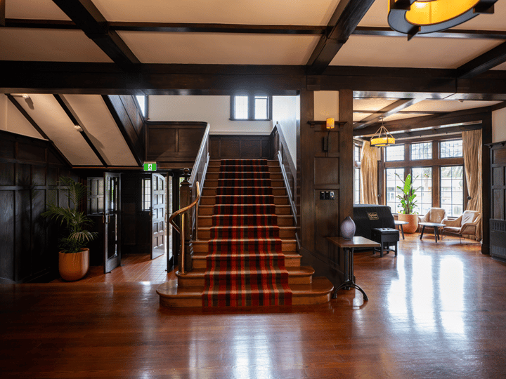 Grand entrance hall with carpeted staircase, dark timber panelling and polished hardwood floor