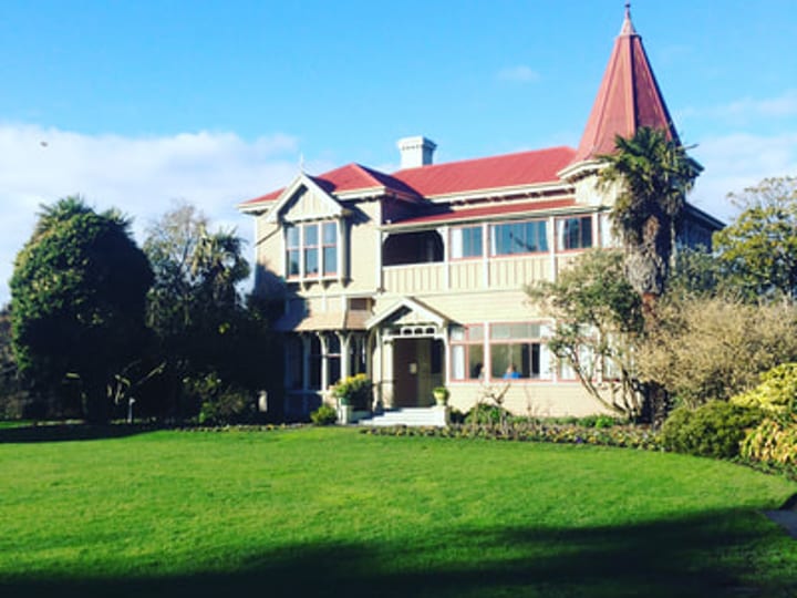Two-storey heritage villa with red-roofed tower, set in a lawn with established trees