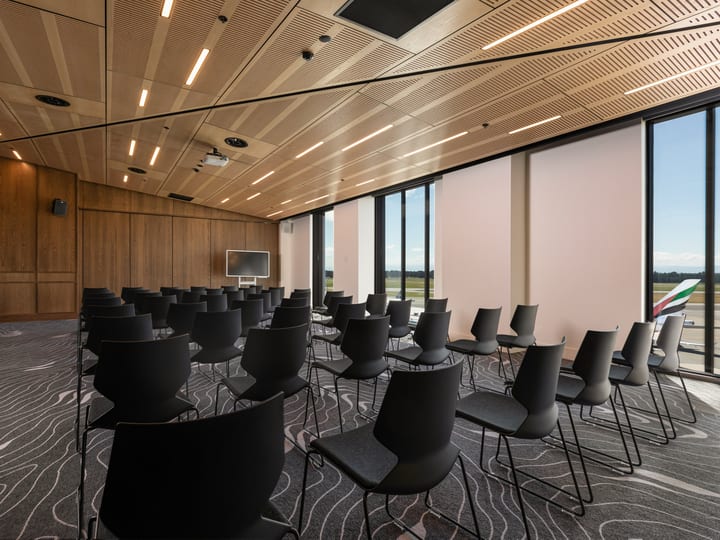 Timber-lined conference room with rows of black chairs, flat screen and large windows on one side