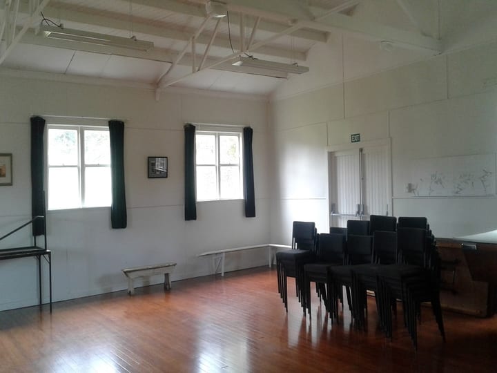 Plain white hall interior with timber floor and stacked chairs