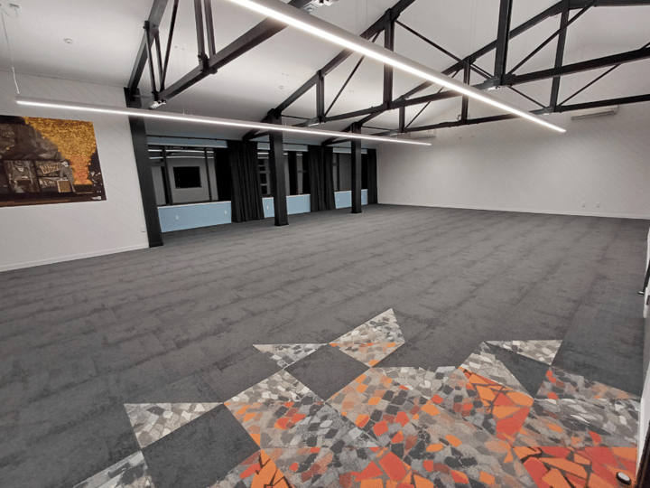Open room with exposed beams, carpet and artwork on white walls