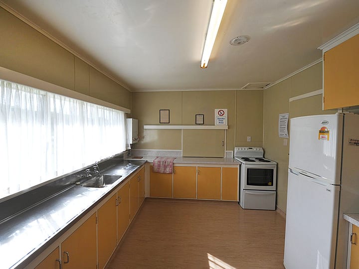 Basic kitchen with orange cabinetry, stove, fridge, and white sheer curtains