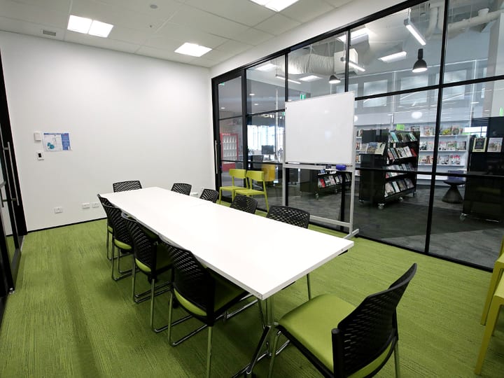 Meeting room with long table, green chairs, whiteboard, and glass wall