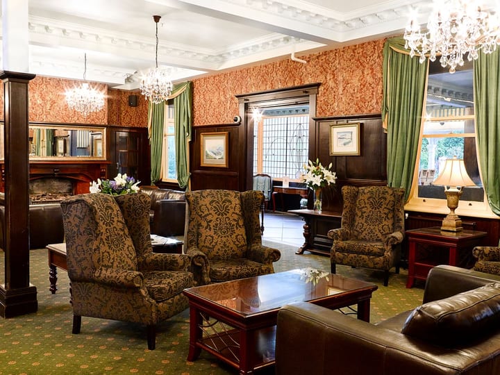 Heritage lounge with patterned armchairs, dark timber columns, crystal chandeliers and decorative wallpaper
