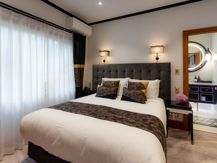 Hotel bedroom with wall sconces, upholstered bedhead, and ensuite glimpse