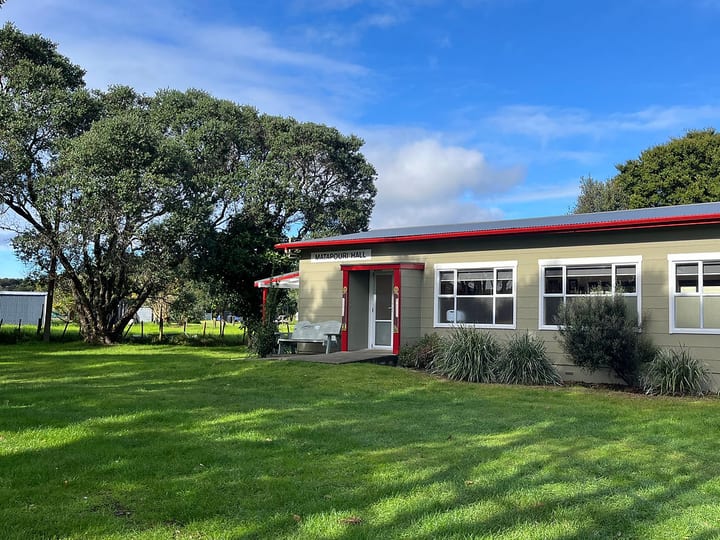 Small rural hall with green cladding, red roof trim, and lawn surrounds