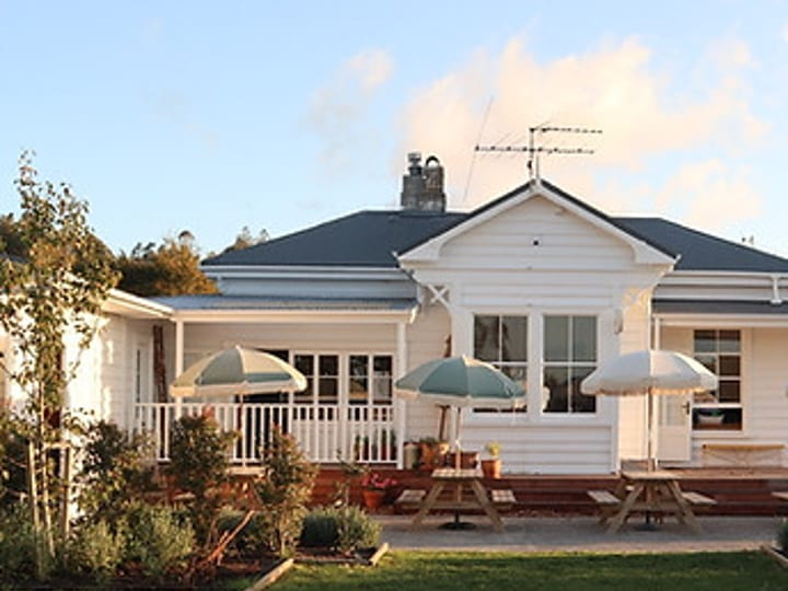 White timber cottage exterior with verandah, outdoor tables and umbrellas, small lawn garden