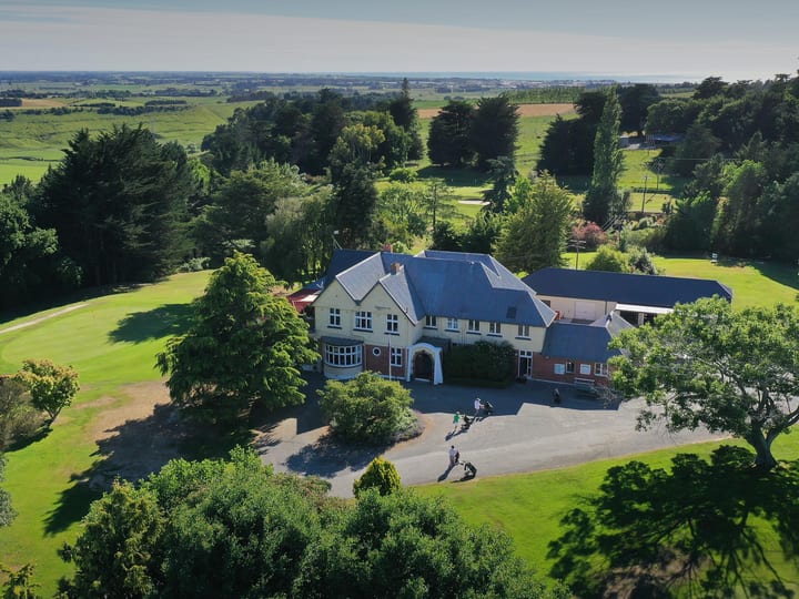 Aerial view of golf clubhouse and grounds amid trees and fairways