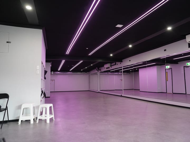 Bare concrete-floored studio with black ceiling, strip LED lighting, and a mirrored wall
