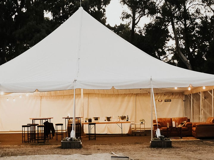 White marquee tent set up on farm grounds at dusk with festoon lights