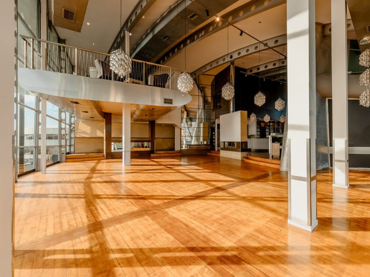 Open event floor with polished timber, curved mezzanine above, spherical pendant lights, floor-to-ceiling glazing