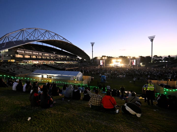 Stadium exterior at dusk with large crowd and concert stage inside