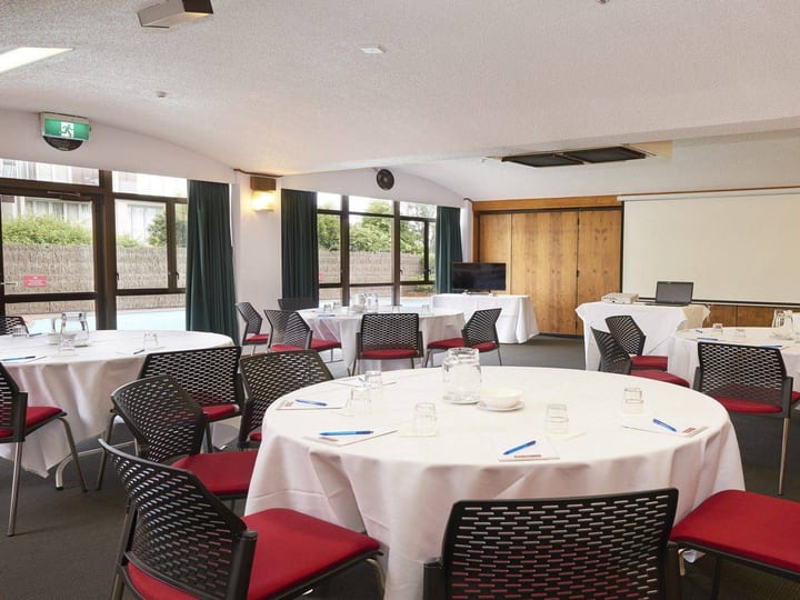 Function room with round tables, timber wall panels and projection screen