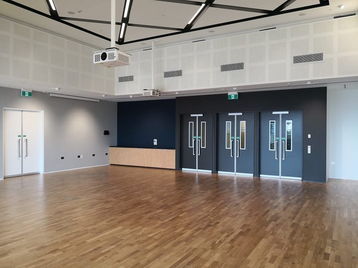 Timber-floored hall with navy doors, geometric black ceiling frame, and movable partition wall