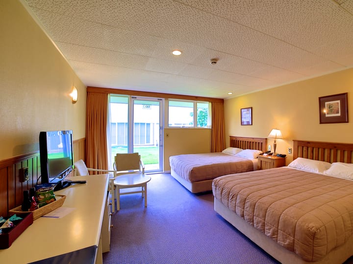 Twin hotel room with two beds, TV and sliding doors to lawn outside