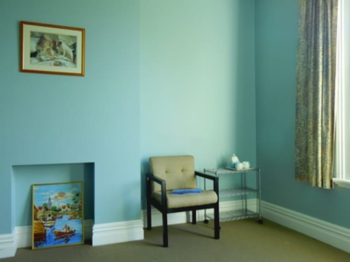 Period room interior with fireplace, armchair, framed prints, and blue-green painted walls