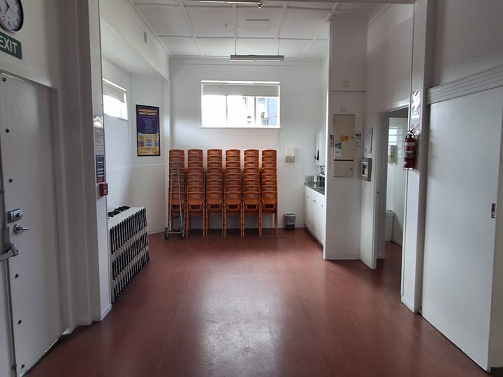 Plain hall with stacked chairs, vinyl floor and small kitchen servery