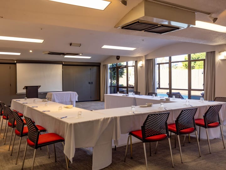 Plain conference room with white tables in U-shape layout, red-seated chairs, and projection screen