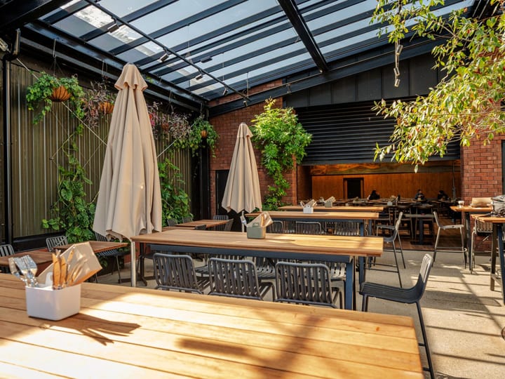Glass-roofed courtyard with timber tables, hanging plants and brick wall, set for dining