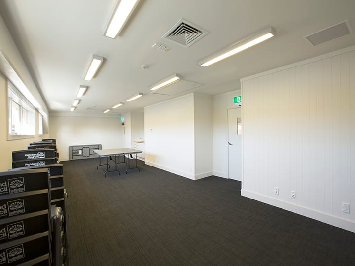 Plain meeting room with dark carpet, folding tables and stacked chairs