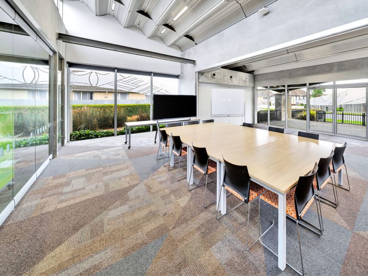 Boardroom with long table, wall-mounted screen, floor-to-ceiling glazing to outdoor area