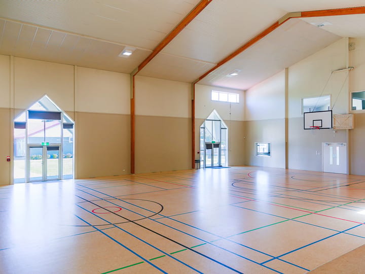 Sports hall interior with court markings, high ceiling, and basketball backboard on far wall