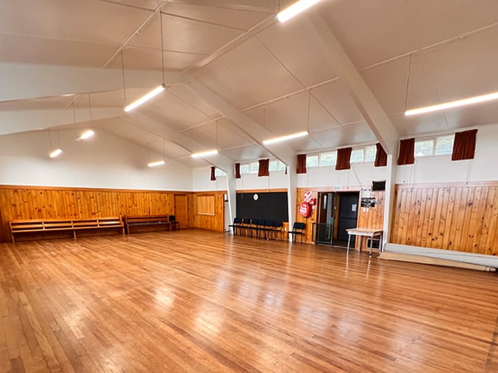 Open timber-floored hall with pine-lined walls, vaulted ceiling, and fluorescent strip lighting