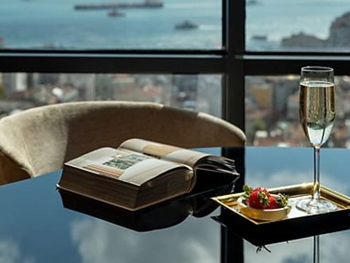 Glossy dark table with champagne glass, book, and small dish beside a panoramic city view