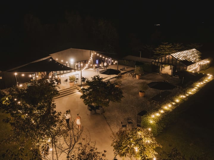 Night aerial of lit venue buildings and string lights on gravel courtyard