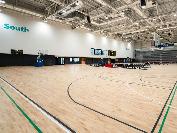 Large indoor sports hall with timber court markings, high ceiling, roof trusses and retractable seating