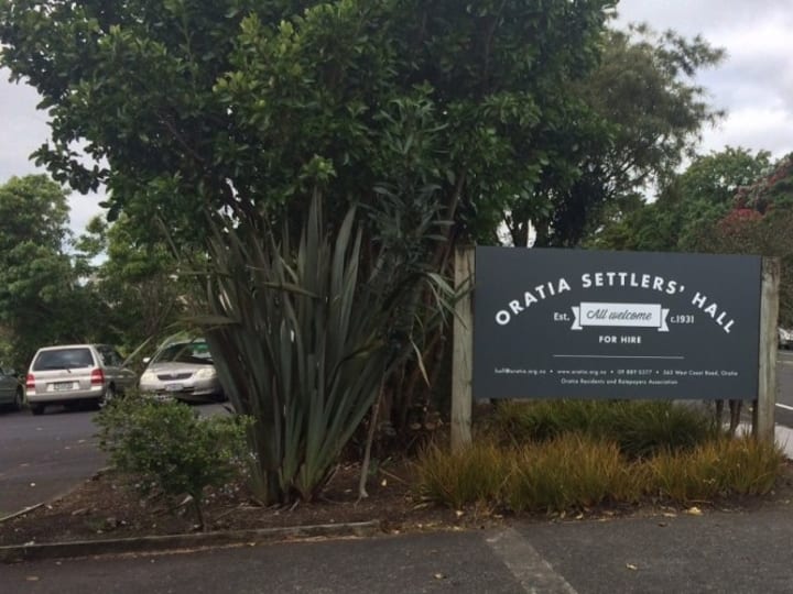Venue sign among trees and plantings beside a road