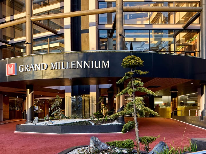 Grand Millennium hotel entrance with curved canopy, timber accents, and sculpted trees