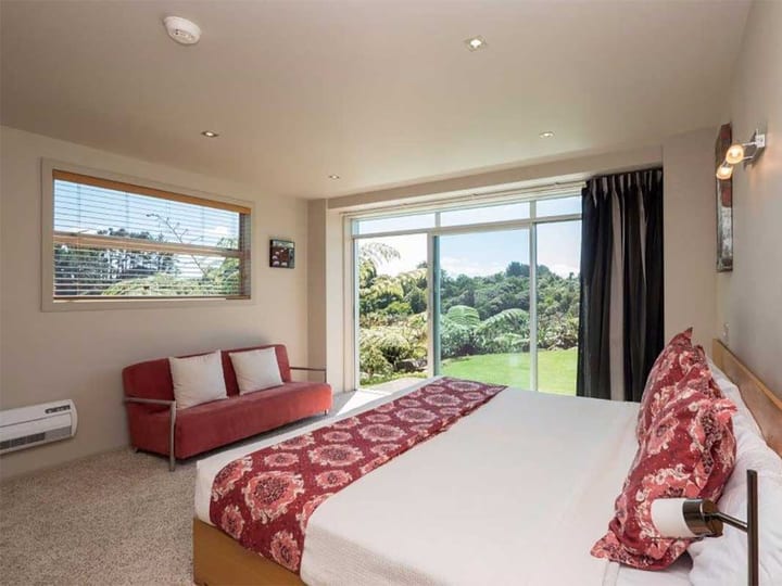 Studio with a king bed, red sofa and sliding doors opening to a garden view