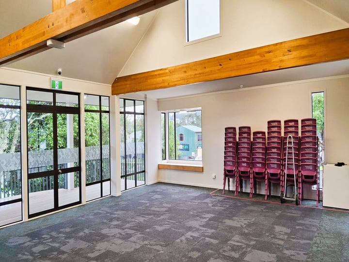 Hall room with vaulted timber-beam ceiling, glass doors, and stacked chairs