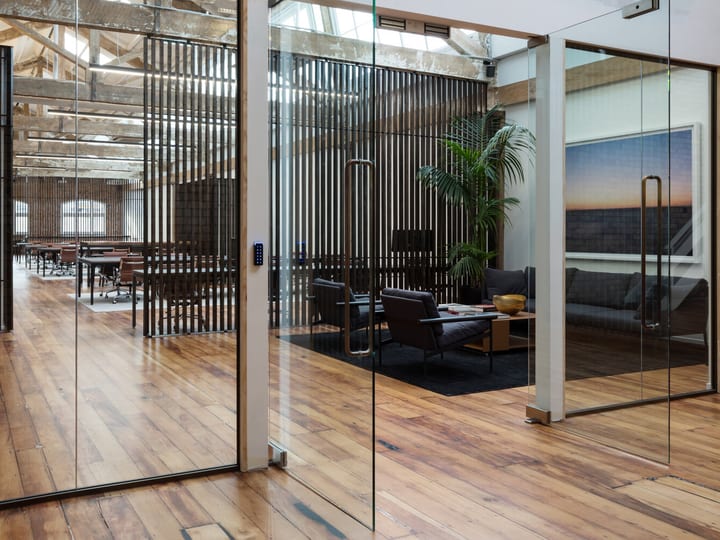 Open-plan loft space with timber floor, vertical slat screens, glass-walled meeting rooms