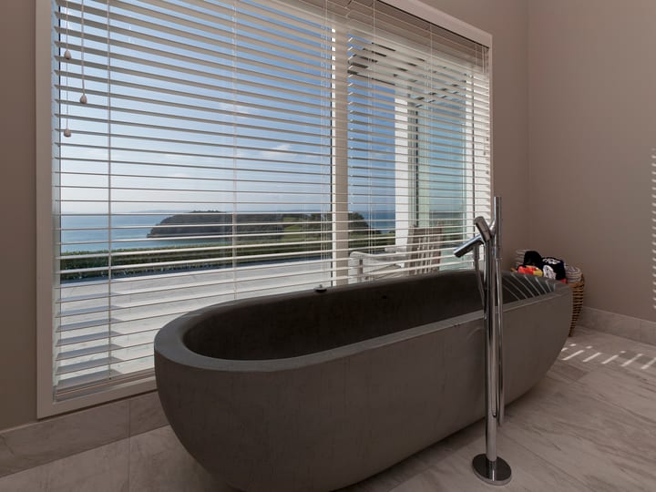 Dark stone bath with floor-mounted tap and large window overlooking sea headland