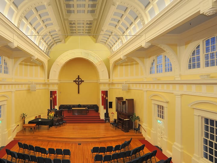 Pale yellow church interior viewed from above showing arched apse, wooden cross, and rows of chairs