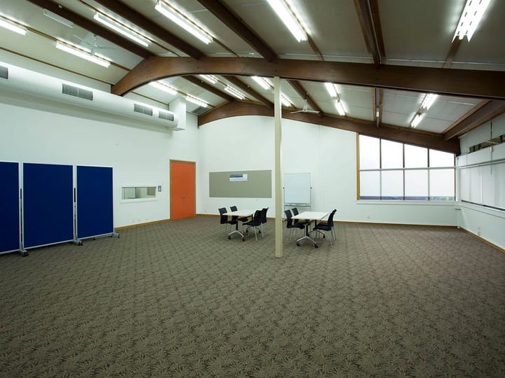 Community hall with curved timber-beam roof, movable partitions, and scattered chairs
